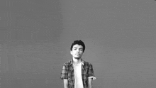 a young man in a plaid shirt is standing in front of a gray background in a black and white photo .