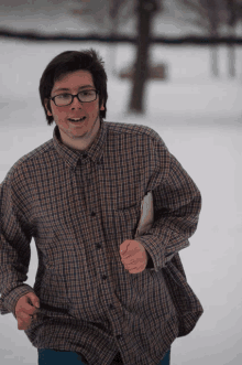 a man wearing glasses and a plaid shirt is running through the snow