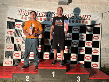 two men stand on a podium in front of a 103 street sports complex sign