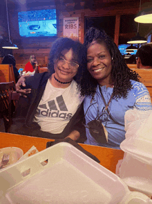 a woman wearing an adidas shirt sits next to another woman at a table