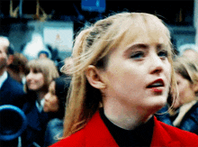 a woman wearing a red jacket stands in a crowd of people