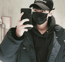 a man wearing a face mask and a hat is taking a selfie with his cell phone .