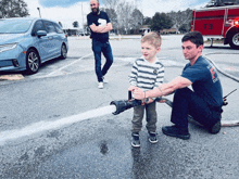 a man in a fireman 's uniform is holding a fire hose while a little boy looks on