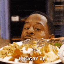 a man is eating a plate of food and saying hungry af .