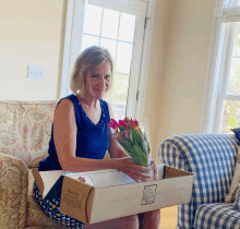 a woman sits on a couch holding a cardboard box that says fragile