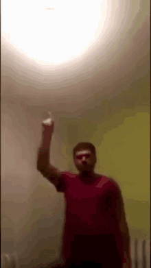 a man in a red shirt is standing in a room holding up his hand