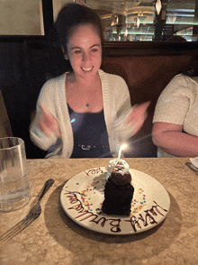 a woman blows out a candle on a birthday cake on a plate with happy birthday written on it