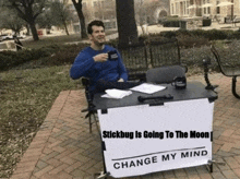 a man is sitting at a table with a sign that says stickbug is going to the moon