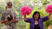 a man with a beard holds a football and a woman holds pink pom poms in front of a duck dynasty logo