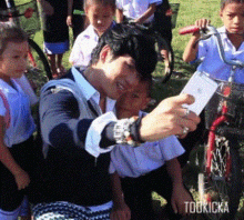 a man is taking a selfie with a group of children and the word toukicka is on the bottom right