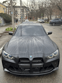 a black bmw is parked in a parking lot in the rain