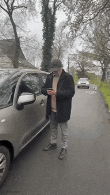 a man is standing next to a car on the side of the road and looking at his phone .