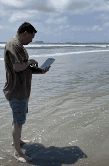 a man standing on the beach using a laptop