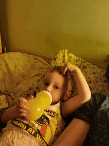 a little boy drinking from a bottle with a shirt that says " hero at work "