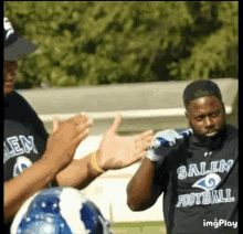 a man wearing a salem football shirt is holding a bat and giving a thumbs up to his teammates .