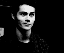 a black and white photo of a young man in a plaid shirt smiling .