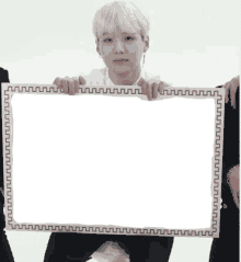 a young man holds a white frame with a black border