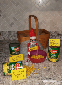 an elf on the shelf is surrounded by cans of corn