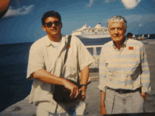 two men are posing for a picture in front of a cruise ship