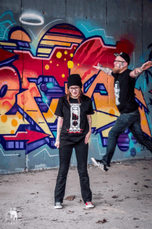 a man and a woman are posing in front of a wall with graffiti on it