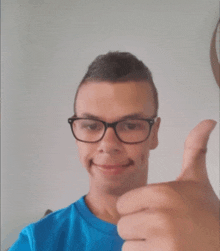 a young man wearing glasses gives a thumbs up