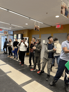 a group of people are standing in a hallway with an exit sign above them