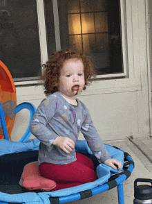 a little girl is sitting on a blue trampoline with chocolate on her face