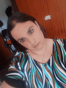 a woman wearing a striped shirt and a cross necklace takes a selfie