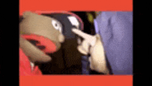 a puppet is wearing a hat and pointing at another puppet .