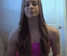 a woman with long hair is wearing a pink tank top and looking at the camera .