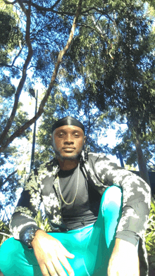 a man sitting under a tree wearing a black shirt and blue shorts