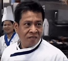 a man in a chef 's uniform is making a funny face while standing in a kitchen .