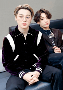 two young men sitting on a couch one wearing glasses