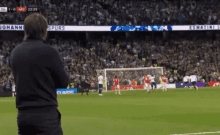 a man watches a soccer game with a score of 1-0