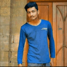 a young man wearing a blue shirt and jeans is standing in front of a wooden door .