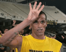 a man wearing a yellow shirt that says thank you is waving his hand