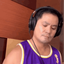 a man wearing headphones and a purple tank top is looking down