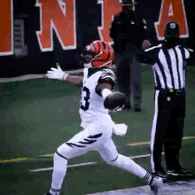 a football player with the number 3 on his jersey is jumping in the air while a referee watches .