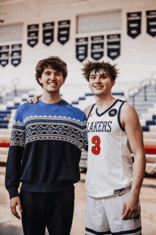 a man in a lakers jersey stands next to a man in a sweater