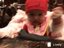 a baby wearing a red hat and a pink bib is sitting on a table with a lively logo on the bottom right