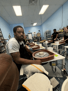 a man in an apron sits at a pottery wheel in a workshop