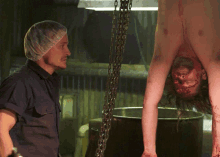 a man standing next to a woman hanging upside down with blood on her face