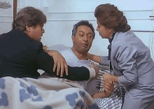 a man is laying in a hospital bed while a woman and a man are standing around him .