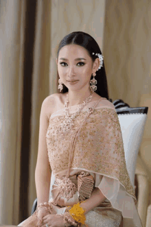 a woman wearing a gold dress and earrings sits on a chair