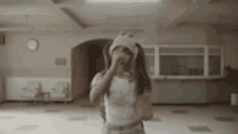 a woman wearing a pigtails hat and a crop top is standing in an empty room .