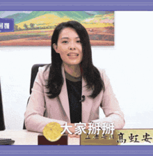 a woman in a pink jacket sits at a desk with a name plate that has chinese characters on it