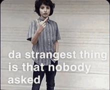 a young boy is giving the middle finger in front of a garage door with the words `` da strangest thing is that nobody asked '' .