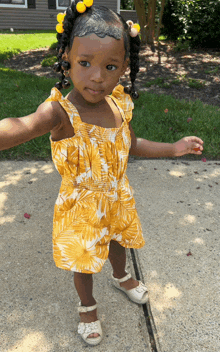 a little girl wearing a yellow jumpsuit and white shoes stands on a sidewalk