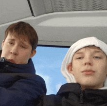 two boys are sitting on a bus and one of them has a white hood on