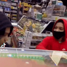 a woman wearing a red hoodie and a black mask is standing in front of a counter in a store .